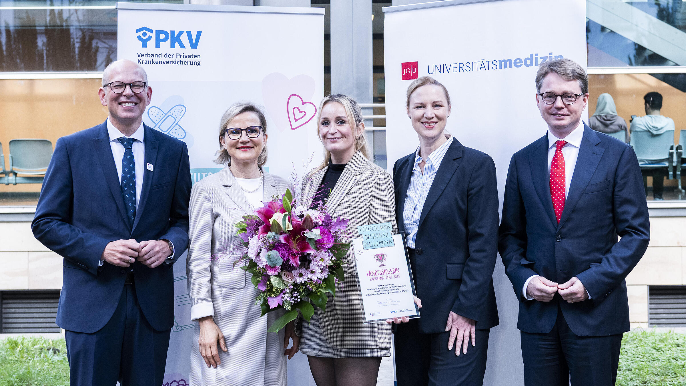 Pflegeprofi Katharina Roos (Mitte) umrahmt von (v.l.n.r.) Univ.-Prof. Dr. Ralf Kiesslich, Vorstandsvorsitzender und Medizinischer Vorstand der Universitätsmedizin Mainz, Univ.-Prof. Dr. med. Annette Hasenburg, Direktorin der Klinik und Poliklinik für Geburtshilfe und Frauengesundheit der Universitätsmedizin Mainz, Dörte Schall, Ministerin für Arbeit, Soziales, Transformation und Digitalisierung des Landes Rheinland-Pfalz sowie Florian Reuther, Direktor des PKV-Verbands